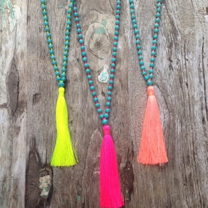May include: Three necklaces with turquoise beads and bright neon tassels. The tassels are yellow, pink, and orange.