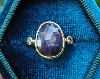 May include: A ring with a large, oval-shaped purple gemstone set in gold. The ring is in a blue velvet ring box.