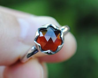May include: A silver ring with a red gemstone set in a flower-shaped setting.