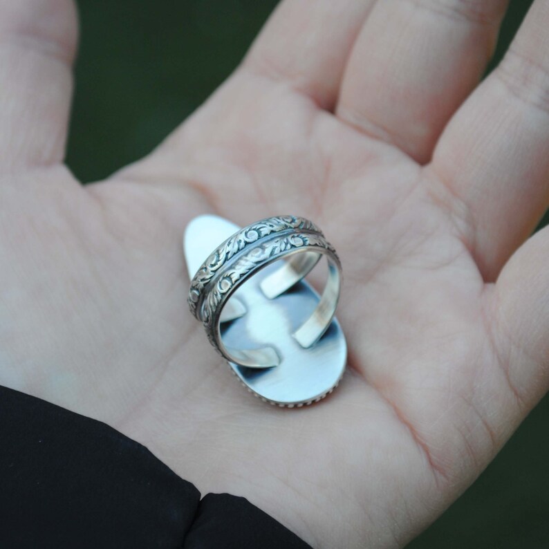 Op de afbeelding: Een zilveren ring met een ovale steen en een gedetailleerd bloemmotief op de band.