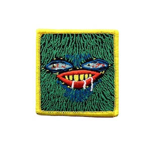 May include: Green embroidered patch with a cartoon face with a large red mouth, yellow teeth, and blue eyes. The face is surrounded by green and black embroidery.