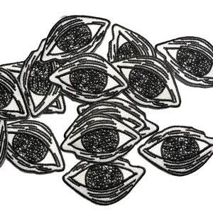 May include: A collection of black and white embroidered iron-on patches featuring a stylized eye design.