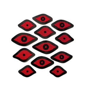 May include: A collection of eleven embroidered eye patches. Each patch features a red eye with a black pupil, outlined in black. The patches are in various sizes and shapes, suitable for clothing or craft projects.