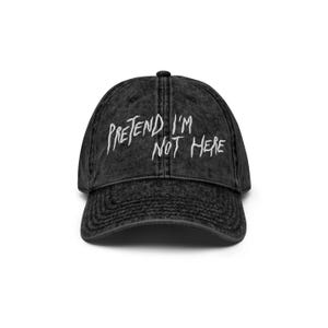 May include: Black distressed denim baseball cap with white embroidered text that reads "Pretend I'm Not Here".