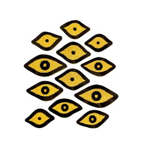 May include: A collection of embroidered eye patches. Each patch features a yellow eye with a black outline and a black pupil. The patches are arranged in a scattered pattern against a white background.