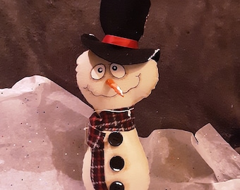 May include: A handmade snowman decoration with a black top hat, red ribbon, and a plaid scarf. The snowman has a carrot nose and black button eyes and buttons. It is mounted on a small wooden base, perfect for winter holiday decor.