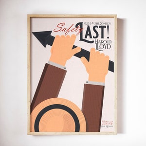 Può includere: Un poster vintage per il film di Harold Lloyd del 1923 "Safety Last!" Il poster presenta un'immagine di un uomo che tiene una grande freccia, con il titolo "Safety Last!" in grassetto rosso e "Harold Lloyd" in rosso più piccolo sotto. Il poster è incorniciato in una cornice di legno chiaro.