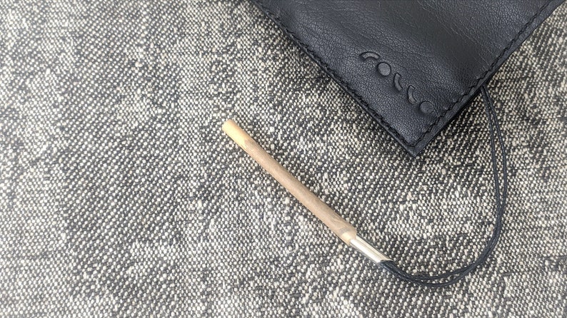 May include: A black leather case with the embossed word "rocco" and a small, cylindrical object with a silver tip. The object is light brown and tan. The items are on a textured gray and white surface.
