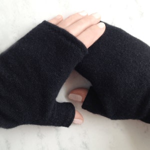 May include: A pair of black fingerless gloves made of a soft, knitted fabric. The gloves are shown on a white marble surface.