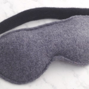 May include: A gray sleep mask with a black elastic band. The mask is made of a soft, fuzzy material.