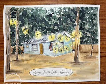 Op de afbeelding: Waterverf schilderij van een blauw huis aan het meer met een veranda lamp en een kleine Amerikaanse vlag aan de zijkant. Het huis is omringd door bomen en heeft een bord met de tekst "Papa Joe's Lake House".