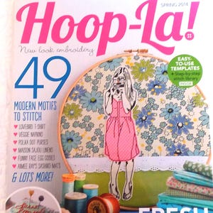 May include: The Spring 2014 issue of Hoop-La! magazine features a cover with a large embroidery hoop displaying a floral pattern and a pink-dressed figure. The text includes 49 Modern Motifs to Stitch, Fresh & Simple Stitching, and Quick-Stitch Fun.