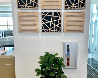 May include: Six square acoustic panels with geometric designs in black and wood tones are mounted on a white wall. A potted green plant sits in front of a silver fire extinguisher cabinet.