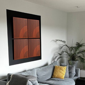 Puede incluir: Un sofá gris con una manta y una almohada amarilla en una sala de estar con suelo de madera. Una estantería negra llena de libros y una mesa auxiliar negra están en el fondo. Una obra de arte enmarcada con un patrón geométrico en tonos marrones está en la pared.