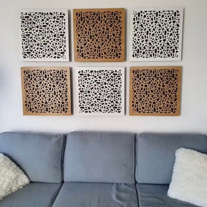 以下が含まれることがあります： 幾何学模様の正方形のアコースティックパネルが6枚。パネルは木でできており、白黒のデザインです。パネルは白い壁にグリッド状に配置されています。