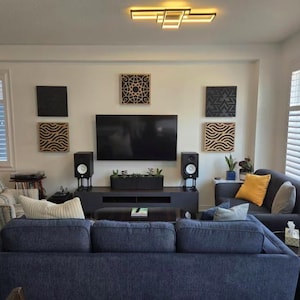 Puede incluir: Un salón moderno con un televisor de pantalla plana montado en la pared. Paneles decorativos de madera con patrones geométricos adornan la pared. Un sofá azul oscuro y dos altavoces negros están frente al televisor.