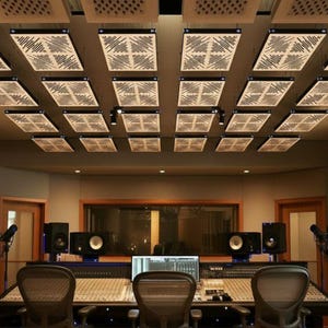 May include: A professional recording studio with soundproofing panels on the ceiling. The room features a mixing console, studio monitors, microphones, and chairs. The lighting is provided by lamps and recessed lights.