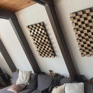 Könnte beinhalten: Zwei rechteckige akustische Diffusorplatten an einer weißen Wand. Jede Platte besteht aus einem Gitter aus hellen Holzblöcken unterschiedlicher Höhe, die eine dreidimensionale, strukturierte Oberfläche mit einem sich wiederholenden geometrischen Muster bilden.