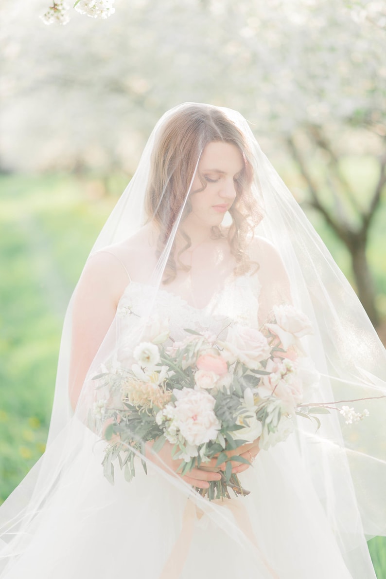 Puede incluir: Una novia con un vestido de novia blanco y velo sostiene un ramo de flores blancas y rosas. El ramo est&aacute; compuesto por rosas, peon&iacute;as y otras plantas verdes.