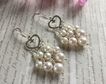 May include: Silver heart-shaped dangle earrings with a cluster of white pearls and small white beads.