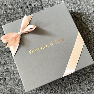 May include: A gray gift box with a pink satin ribbon and bow. The box has the text "Florence & Tilly" printed in gold on the front.