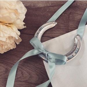 May include: A silver horseshoe with a blue ribbon tied around it. The horseshoe has an inscription on it.