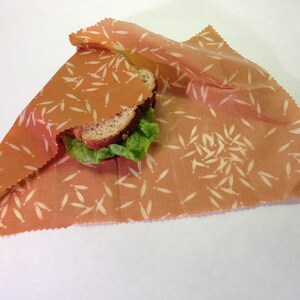 Peut inclure: Un sandwich envelopp&eacute; dans une pellicule alimentaire r&eacute;utilisable avec un fond brun et un motif blanc de petites feuilles.