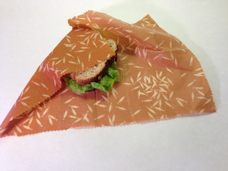 Peut inclure: Un sandwich envelopp&eacute; dans une pellicule alimentaire r&eacute;utilisable avec un fond brun et un motif blanc de petites feuilles.