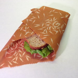 Peut inclure: Un sandwich envelopp&eacute; dans une pellicule alimentaire r&eacute;utilisable brune avec un motif de poisson blanc. Le sandwich est compos&eacute; de pain complet, de laitue et d'une tranche de fromage.