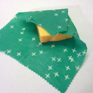 Peut inclure: Un tissu vert &agrave; motif de croix blanches est envelopp&eacute; autour d'un bloc de fromage jaune.