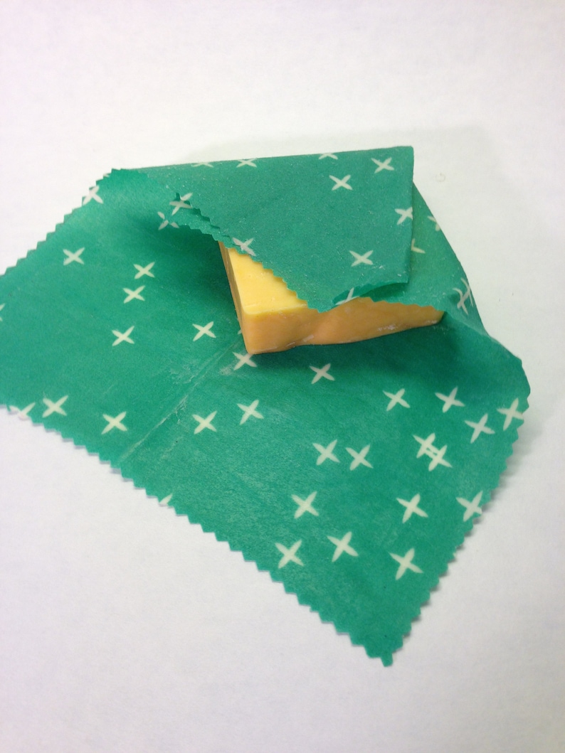Peut inclure: Un tissu vert &agrave; motif de croix blanches est envelopp&eacute; autour d'un bloc de fromage jaune.