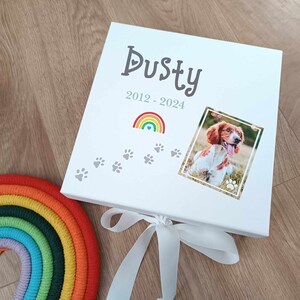 May include: White keepsake box with a rainbow, paw prints, and a photo of a dog. The box is decorated with the text "Dusty 2012-2024".