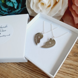 Peut inclure: Deux colliers en argent avec des pendentifs en forme de cœur. Un pendentif dit "Ensemble" et l'autre dit "Pour toujours". Les colliers sont dans une boîte blanche.