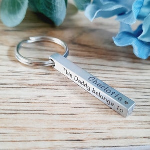 Può includere: Portachiavi in ​​argento con un ciondolo a forma di barra inciso con il testo "Charlotte This Daddy belongs to" e un piccolo simbolo di cuore.