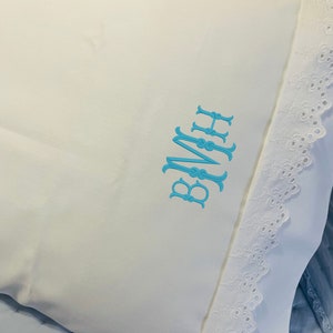 May include: White pillow with a blue embroidered monogram "BMH" and a white lace trim.