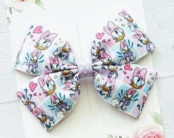 May include: A hair bow made of grosgrain ribbon featuring a repeating pattern of Daisy Duck, pink hearts, and blue question marks on a pastel plaid background. The center is a light purple band with white polka dots, attached to a display card.