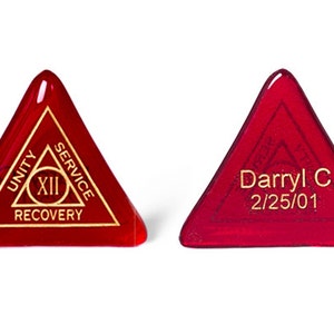 May include: Two red triangular glass tokens with gold lettering. One token has the words "Unity", "Service", "Recovery" and "XII" inscribed on it. The other token has the name "Darryl C." and the date "2/25/01" inscribed on it.