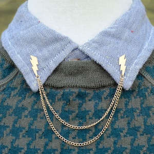 Peut inclure: Un fermoir de collier en chaîne dorée avec des breloques en forme d'éclair. La chaîne est à double brin et les breloques sont attachées aux extrémités de la chaîne.