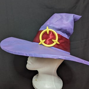 May include: A purple and red wizard hat with a gold starburst design. The hat is on a white mannequin head.