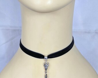 May include: A black velvet choker necklace with a silver-toned pendant. The pendant features a decorative design with a spike at the bottom. The necklace is displayed on a mannequin.