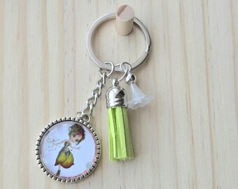 May include: A silver-toned metal keychain featuring a circular pendant with a printed illustration of a figure in a green dress, a bright lime green suede tassel, and a small translucent white flower-shaped charm attached to a split ring.