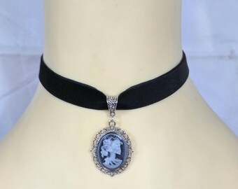 May include: Black velvet choker necklace with a silver-toned pendant. The pendant features a cameo design with a profile of a woman in a silver filigree frame. The necklace is displayed on a mannequin.