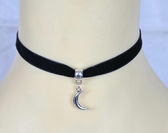 May include: Black velvet choker necklace with a silver crescent moon pendant. The choker is a simple band, and the moon charm hangs from a small silver loop. The necklace is displayed on a mannequin.