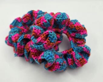 May include: A pair of handmade crochet scrunchies in vibrant colors. The scrunchies feature a mix of blue, pink, and orange yarn, creating a textured and colorful accessory. These scrunchies are perfect for adding a pop of color to any hairstyle.