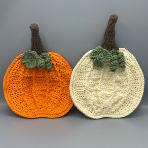May include: Two crocheted pumpkin pot holders, one orange and one white, with brown stems and green leaves.