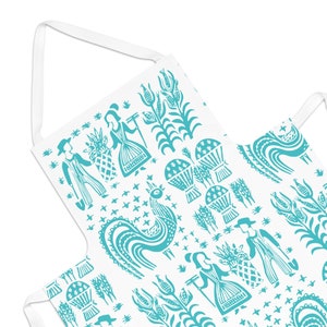 May include: White apron with a repeating teal folk art pattern featuring stylized figures, plants, and a rooster. The apron has a white strap for the neck and ties. The design is reminiscent of traditional folk art.