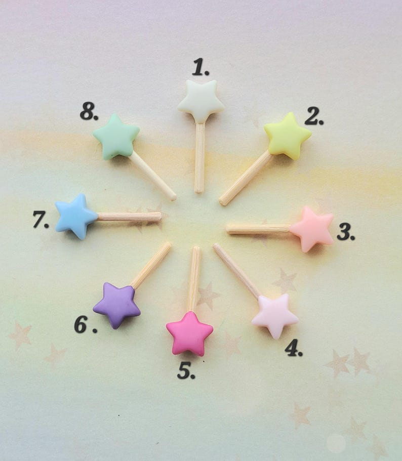 May include: Eight star-shaped toppers on wooden sticks arranged in a circle, numbered 1 through 8. The stars are in various pastel colors including white, yellow, pink, light pink, light purple, purple, blue, and mint green, each with a wooden stem.