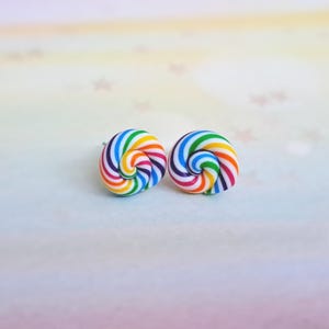 K&ouml;nnte beinhalten: Ein Paar Ohrstecker mit Regenbogenwirbel. Die Ohrringe sind aus Polymer Clay gefertigt und haben einen wei&szlig;en Hintergrund mit Regenbogenstreifen.