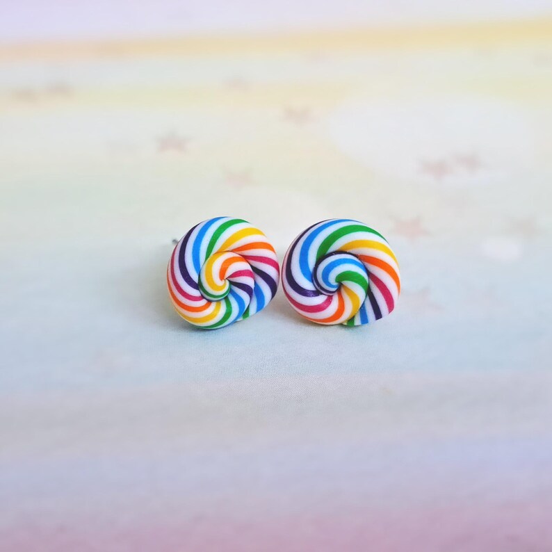 K&ouml;nnte beinhalten: Ein Paar Ohrstecker mit Regenbogenwirbel. Die Ohrringe sind aus Polymer Clay gefertigt und haben einen wei&szlig;en Hintergrund mit Regenbogenstreifen.