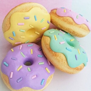 May include: Four mini donuts with different colored frosting and sprinkles. The donuts are yellow, pink, green, and purple.